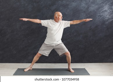 Sporty Elderly Guy Practicing Yoga Indoors. Senior Man Doing Stretching Exercise, Black Background. Active Lifestyle And Healthcare In Any Age, Copy Space