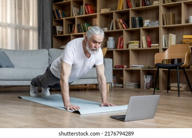 Sporty Elderly Man In Sportswear Planking On Yoga Mat At Home, Watching Fitness Video On Laptop, Living Room Interior, Copy Space. Online Fitness Class, Sports Lifestyle For Seniors Concept