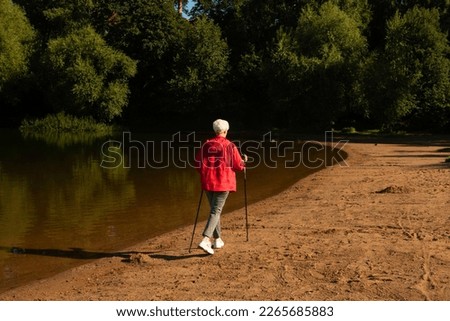 Sporty elderly woman trains endurance while Nordic walking in nature