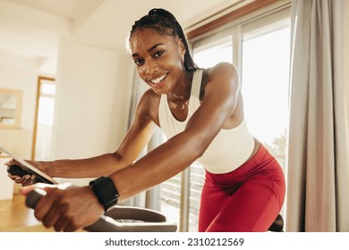 Sporty and enthusiastic young woman happily reaching her fitness goals with the help of her home cycling equipment, determined to achieve her fitness objectives and live a healthy lifestyle. - Powered by Shutterstock