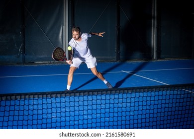 Sporty european man in white t-shirt playing padel tennis indoor