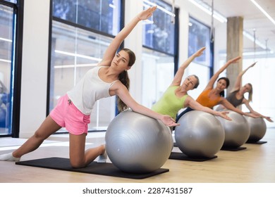 Sporty european woman doing exercises with pilates ball during group training at gym indoor