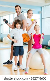 Sporty family. Happy family holding different sports equipment while standing close to each other in health club 