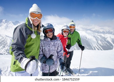 A sporty family of skiers standing in row together on top of the mountain while smiling at the camera as they get ready adventure trip