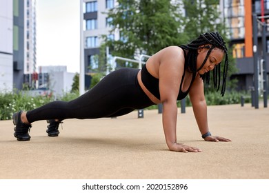 Sporty fat lady in black sportswear, practicing fitness, doing Push ups or press ups exercise, beautiful woman working out outdoors. young overweight woman training alone, side view. copy space