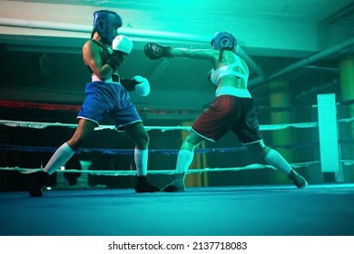 Sporty female boxers improving punches on ring. Two girls in sportswear boxing in blue light on ring, making quick blows watching each others hands and reaction. Sport activity, womens boxing concept - Powered by Shutterstock