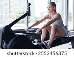 Sporty female using a rowing machine during cross fit training. Female athlete exercising intensely in the gym. High quality photo