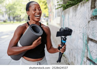 Sporty female vlogger holding her camera and exercise mat in the city
 - Powered by Shutterstock