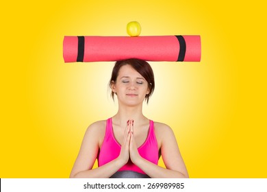 Sporty fit healthy smiling beautiful woman, red head girl holding  an yoga mat on head and apple.Exercise, fitness.Woman standing holding yoga mat isolated on yellow background.
