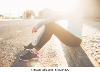 Sporty and fit woman sitting on the street, resting after nice run workout. Urban sport