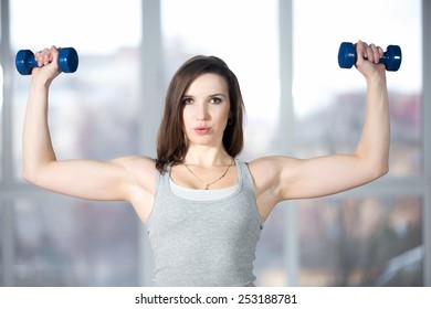 Sporty girl athlete leading active lifestyle, doing fitness training for biceps in grey sportswear with dumbbells, lifting weights, warming up, breathing, exhaling, exhausted