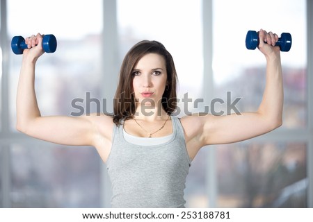 Sporty girl athlete leading active lifestyle, doing fitness training for biceps in grey sportswear with dumbbells, lifting weights, warming up, breathing, exhaling, exhausted