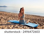 A sporty girl does yoga and fitness on a sandy beach. Does exercises for the back and arms.