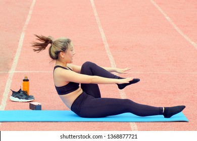 Sporty girl doing leg stretching sitting on a fitness Mat. Group and individual sport activities in the fresh air. Stretching. Fitness at the stadium.