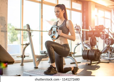 Sporty girl doing lunges with weight plate in the gym