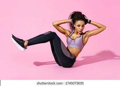 Sporty girl doing twist abs exercise with raised legs. Photo of african american girl in black sportswear on pink background. Strength and motivation