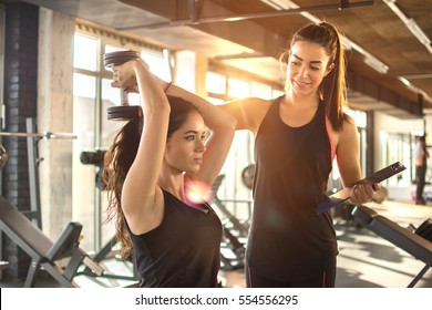 Sporty girl doing weight exercises with assistance of her personal trainer at gym.