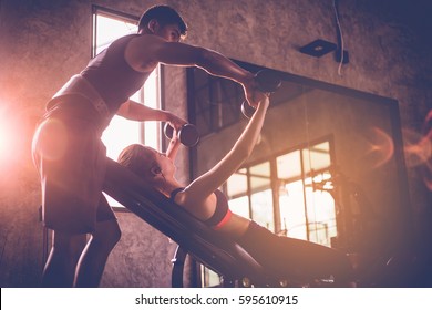 Sporty girl doing weight exercises with assistance of her personal trainer at public gym. - Shutterstock ID 595610915