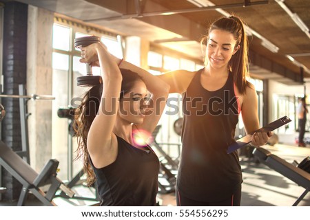 Sporty girl doing weight exercises with assistance of her personal trainer at gym. 商業照片 © 