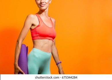 Sporty Girl Holding Yoga Mat Wearing Pants And Bra Over Vibrant Orange Background. Fashion, Sport And Healthy Lifestyle Concept