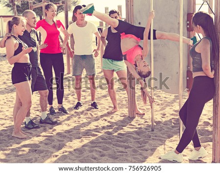 Sporty girl performing pole exercises causing admiration of people watching her