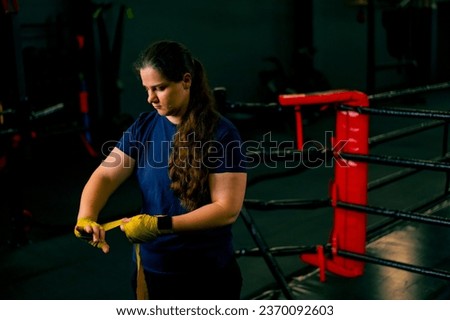 Sporty girl with strong arms prepares for a hard workout wraps a bandage on her fists to protect her fingers in gym
