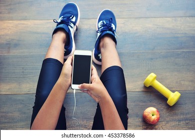 Sporty Girl Using Mobile Phone Sitting On Gym Floor.