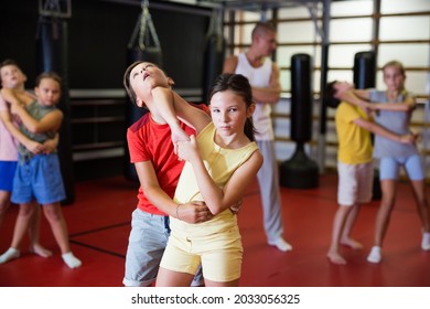 Sporty girls and boys are practices self-defence moves in pairs in sporty gym.