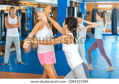 Sporty girls in pairs are training self-defence moves in gym with instructor