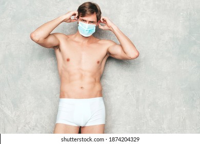 Sporty handsome strong man. Healthy athletic fitness model posing near gray wall in white underwear. Confident sexy fashion male with naked nude torso. Wearing protective mask for corona virus