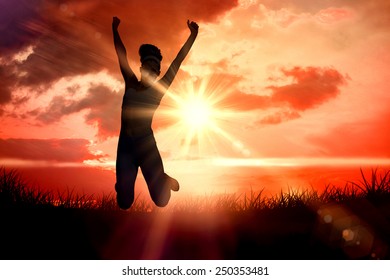 Sporty happy blonde jumping against sunrise over grass