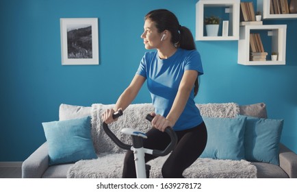 Sporty happy girl training on exercise bike at home listening music looking aside, healthy life - Shutterstock ID 1639278172