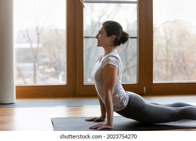 Sporty happy millennial Indian woman practice yoga do stretching or pilates on mat at home. Healthy smiling young mixed race female meditate perform morning exercises train in sportswear indoors.