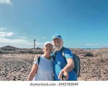 Sporty happy senior couple take a selfie in outdoors on a sunny day walking along a coastal path towards a lighthouse, peaceful and healthy retired lifestyle - Powered by Shutterstock