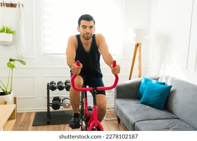 Sporty hispanic man looking happy and with a lot of motivation using his stationary bicycle to workout at home - Shutterstock ID 2278102187