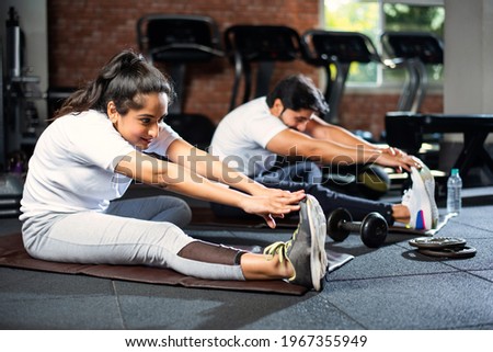 sporty Indian asian young couple stretching in gym post exercise for cooling down, improving flexibility