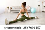 Sporty Indian woman sitting in splits, stretching legs at home, full length portrait. Charming Asian lady doing flexibility exercises, keeping active and strong during covid lockdown