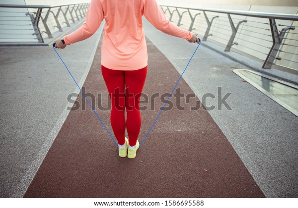 Sporty lady using jumping rope for morning training\
on the bridge stock\
photo