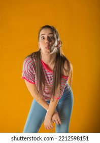 Sporty Lovely Girl In Tank-top And Denim Shorts Dancing With Pleasure And Smiling. Indoor Portrait Of Stunning Female Model With Vintage Hairstyle Waving Hands On Yellow Background.