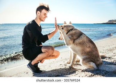 sporty male playing with two husky dogs on beach