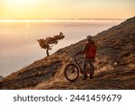 Sporty man athlete is standing with mtb bike at mountaintop and enjoys sunset or sunrise
