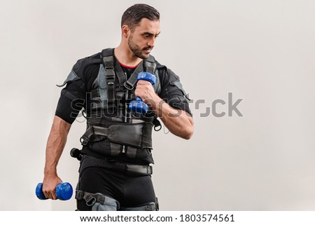 Sporty man in electrical muscular stimulation suit doing exercise with dumbbells