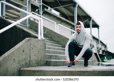 Sporty Man Getting Ready For Winter Urban Running And Outdoor Fitness Workout. Sportsman Lacing Sport Shoes On Wet Stairs.