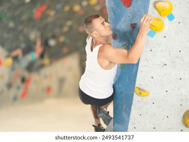 Sporty man grabbing ledges of artificial climbing wall in bouldering centre - Powered by Shutterstock