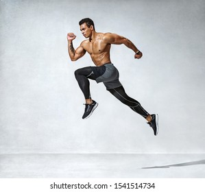 Sportlicher Mann springt. Foto von aktivem Mann mit nacktem Torso auf grauem Hintergrund. Dynamische Bewegung. Seitenansicht. Sport und gesunder Lebensstil