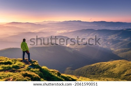 Sporty man on the mountain peak looking on mountain valley with sunbeams at colorful sunset in autumn in Europe. Landscape with traveler, foggy hills, forest in fall, amazing sky and sunlight in fall Foto stock © 