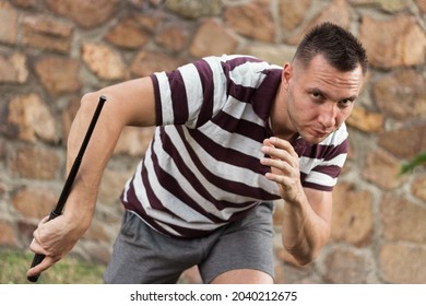 sporty man with police baton performing self-defense maneuver in martial arts against masonry background - Powered by Shutterstock