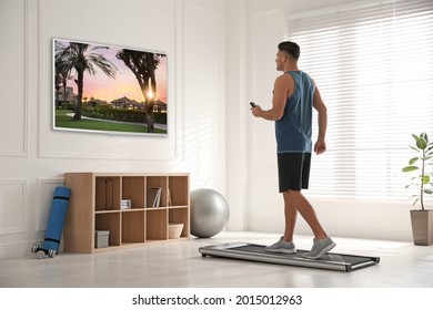 Sporty Man With Remote Control Training On Walking Treadmill And Watching TV At Home