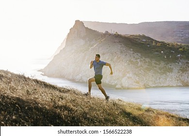 Sporty Man Running Mountain Trail In Uphill At Sunset And Sunlight