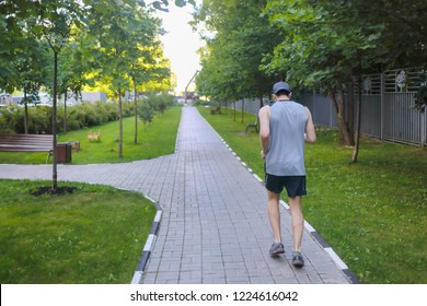 Sporty Man In Shorts And Cap Runs In Green Garden At Summer Day, Back View